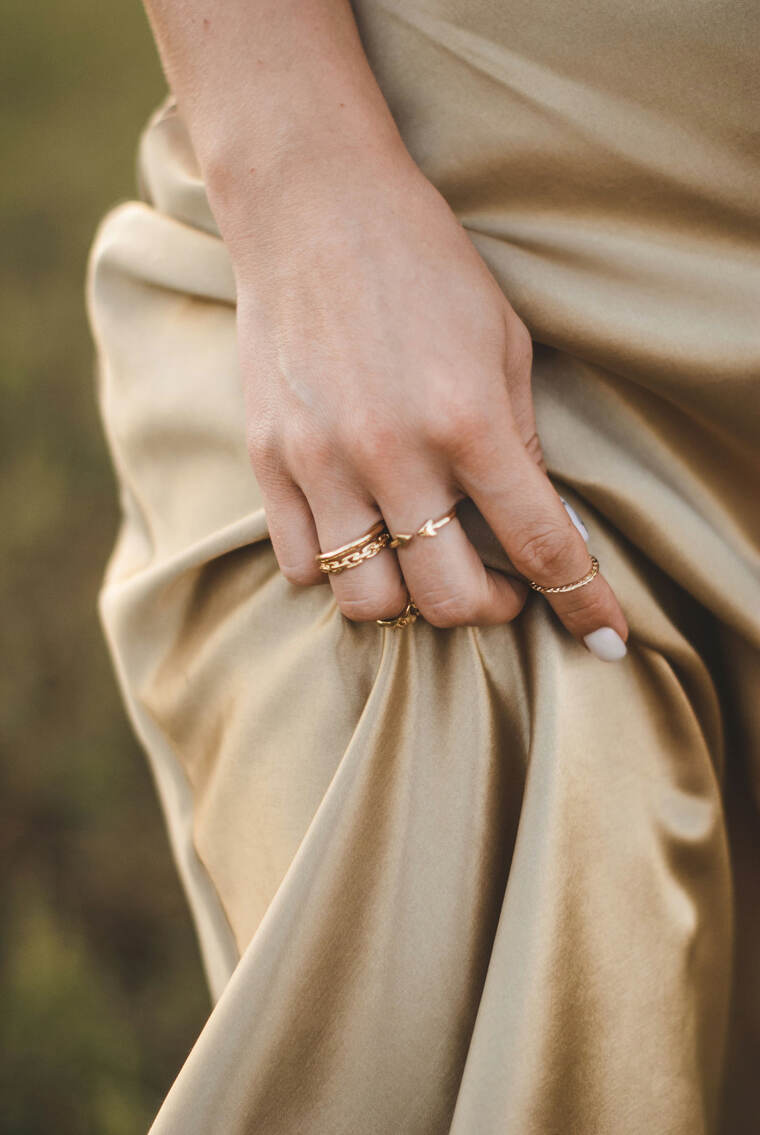 Stacked fine gold rings on a hand gathering champagne satin